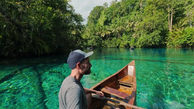 Man boating on a turquoise lake in a tropical rainforest in Paisu Pok, Banggai
