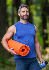 Fototapeta premium Fit your body. Yoga coach. Sport man ready for workout. Healthy lifestyle. Fitness and sport. Yoga mat for training. Sportsman in forest. Man in sportswear with fitness mat outdoor. Regular exercise