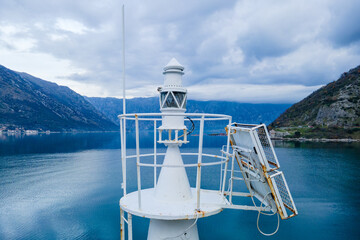 A small white navigation beacon with a solar panel stands on a buoy in a calm mountain bay under cloudy sky, marking a safe route for boats. © Masarik