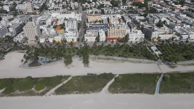 Aerial sweep across miami beach rooftops bordering a sunlit dune corridor