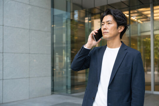 オフィスビル前でスマートフォンで通話する男性