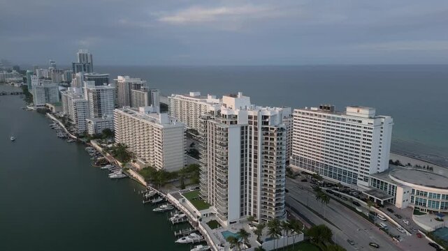 Aerial glide over miami beach towers between an overcast sky and calm waterway
