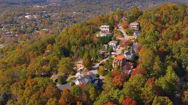 Scenic hillside homes near Asheville, North Carolina surrounded by colorful forests. Aerial view of peaceful mountain living during fall season.