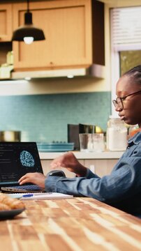 Vertical video: Remote worker uses AI-powered software and laptop with artificial intelligence, neural networks and machine learning for data analysis, while woman telecommutes at home.