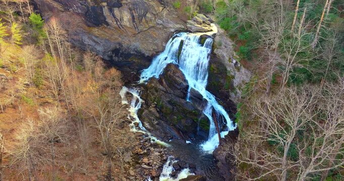 Scenic view of Cullasaja Falls in fall season. Cascading water tumbles over rugged rocks amid vibrant yellow and orange forest trees