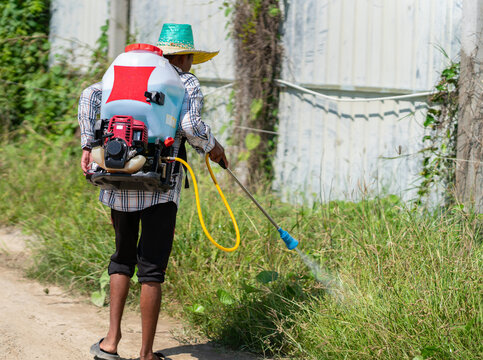Farmer spraying pesticide or herbicide on overgrown grass using a motorized backpack sprayer outdoors.