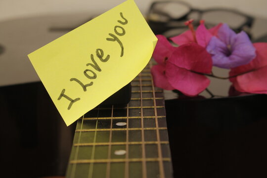 Nota de amor escrita sobre las cuerdas de una Guitarra con un fondo desenfocado.