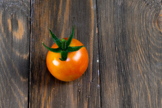 A ripening tomato on a rustic wooden surface with space for text.