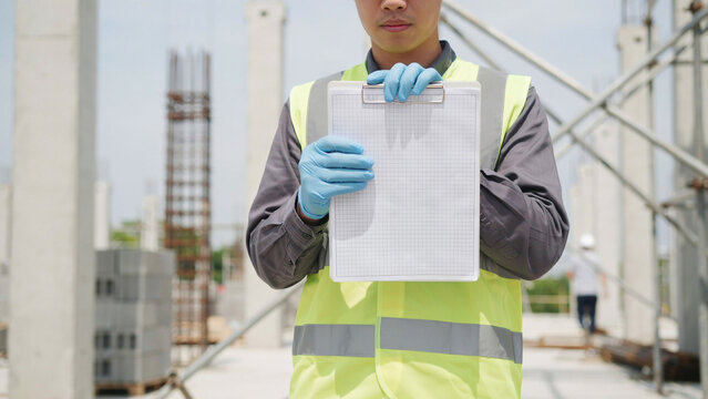 Construction engineer in safety vest holding blank clipboard for copy space at building site