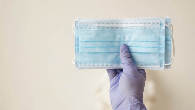 Healthcare worker hand in protective glove holding stack of disposable medical face masks