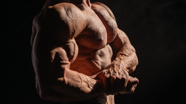 A male bodybuilder poses in shorts, showing off his muscles. Close-up of his chest and abs.