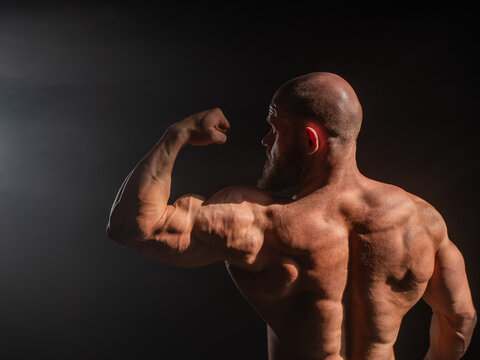 A male bodybuilder poses in shorts, showing off his back muscles.