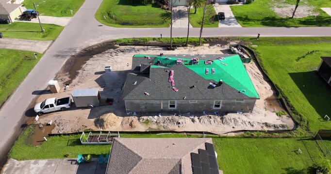 Workers covering private house with asphalt shingles. Rooftop installation project in Florida home construction.