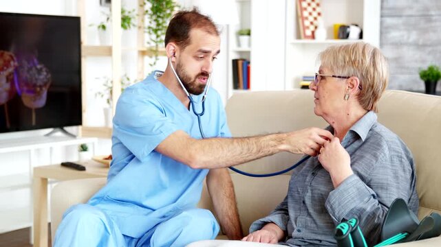 From the side a male nurse listens to a senior woman's chest with a stethoscope, representing routine checkups, preventive care and senior healthcare.