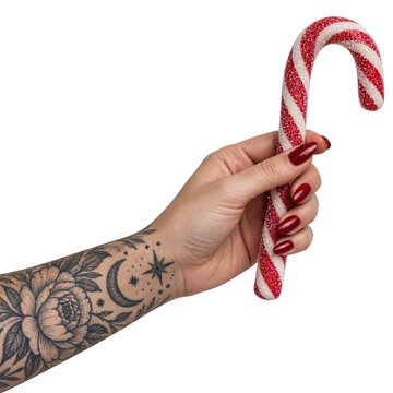  tattooed hand with red manicured nails holds a red and white striped candy cane against a black background.