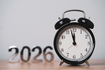 Black alarm clock near midnight with blurred 2026 numbers, symbolizing New Year countdown, year end...