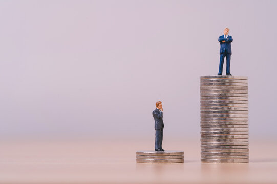Income inequality concept with miniature businessmen standing on different stacks of coins symbolizing wealth gap, salary disparity, financial inequality, career success and economic opportunity.