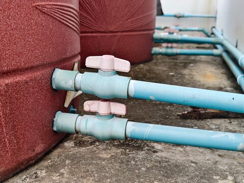 Close-up of double PVC ball valves on blue pipes installed on red domestic water storage tanks for home plumbing and water supply management concepts.
