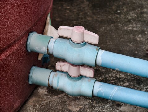 A close-up shot of two blue PVC ball valves with white handles installed on water pipes, connected to the side of a large reddish-brown domestic water storage tank.