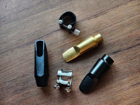 A top-down shot of saxophone and clarinet mouthpieces, both plastic and metal, along with their matching ligatures, neatly arranged on a wooden table. Perfect for music instrument accessory listings.