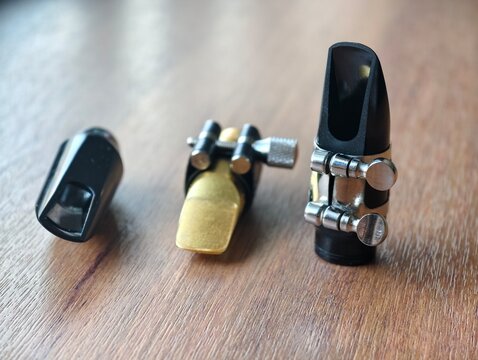 Close-up view of a selection of plastic and metal saxophone and clarinet mouthpieces with ligatures on a wooden surface. Ideal for music shop displays, gear reviews, and equipment guides.