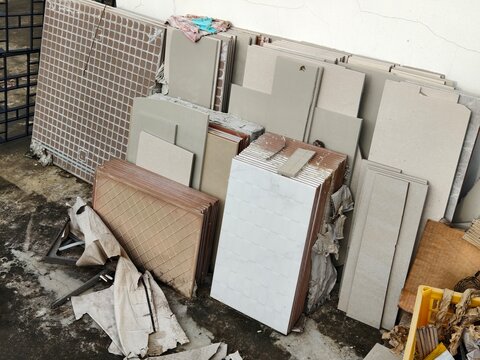A pile of leftover ceramic floor and wall tiles stacked against a concrete wall. Ideal for home renovation, building materials, construction site cleanup, and DIY concepts.