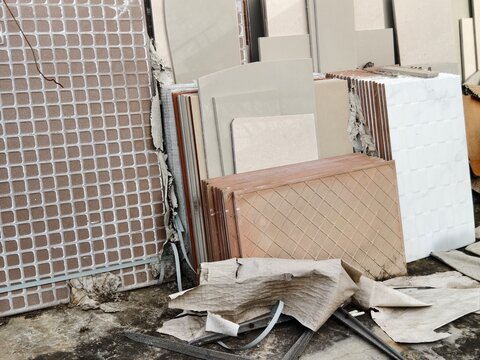 A close-up shot of various types of ceramic and porcelain tiles, both old and new, neatly stacked and leaned against a concrete structure at a building site or home renovation project.