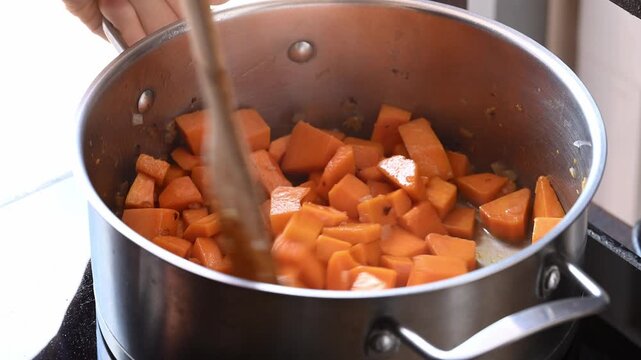 Stirring butternut squash in a pot to make butternut squash soup, homemade food in autumn