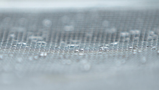 Close up of water droplets on a fine metal mesh screen texture.A high-quality close-up macro photograph capturing clear water droplets and condensation resting on a fine stainless steel 