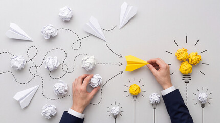 Fototapeta premium Creative business strategy and innovation concept with hands holding a yellow paper plane and crumpled papers transformed into light bulbs representing successful solution and new ideas.