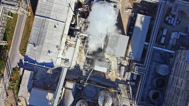 Several structures and equipment are visible at an industrial site. Steam rises from one section, showing ongoing activity in the factory during daylight.