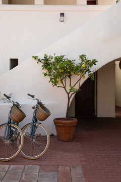 bicycles with rattan baskets for guests parked in the courtyard of a spanish-style boutique hotel with white walls, arches, and brick floor