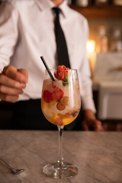 bartender about to grab cocktail with floral garnish and straw off the bar counter 