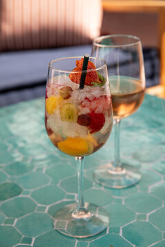 high angle shot of cocktail garnished with florals in a wine glass with straw next to glass of wine on a turquoise tile surface in an ourdoor upscale bar or restaurant patio