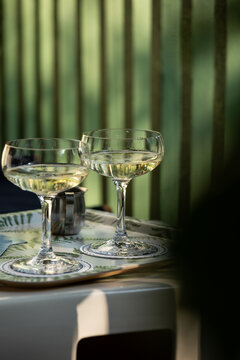 moody image of 2 coupe glasses of champagne on a tray during late afternoon with shadows against a green architectural wall