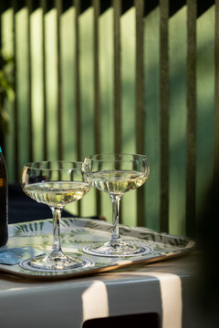 moody image of 2 coupe glasses of champagne on a tray during late afternoon with shadows against a green architectural wall