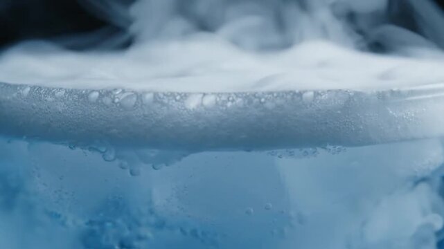 Close up of dry ice sublimating in water with dense white smoke and bubbles.