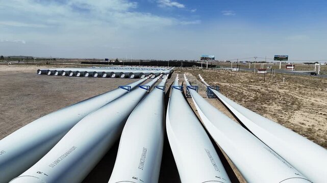Large wind power blades stacked neatly outdoors under blue sky