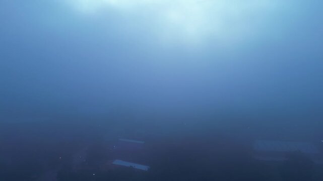 An aerial view looking down upon a dense, dark sea of ​​clouds, with scattered white clouds drifting across the sky, contrasting with the deep blue of the early morning and the soft, gentle light.