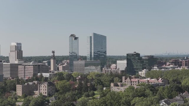 White Plains downtown towers rise above the leafy urban foreground, Westchester County, New York. The aerial camera travels west, climbing. Green foliage forms a textured pattern across the landscape.