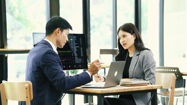 Asian financial professionals discussing investment strategies and market trends while reviewing stock charts and financial data in a modern office.