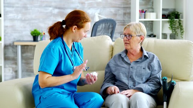 Female nurse discusses medication dosage with a senior woman in residential care, supporting patient education and safe medication management.