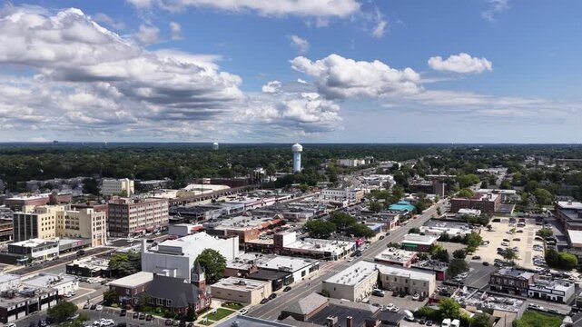 Railway tracks and roads cross the center of Rockville Centre, Nassau County, Long Island, New York. The drone travels northeast, climbing. Green foliage forms a textured pattern across the landscape.