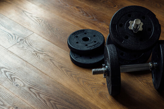 Black adjustable dumbbells and weight plates on a wooden floor background with copy space for fitness training design. Horizontal format