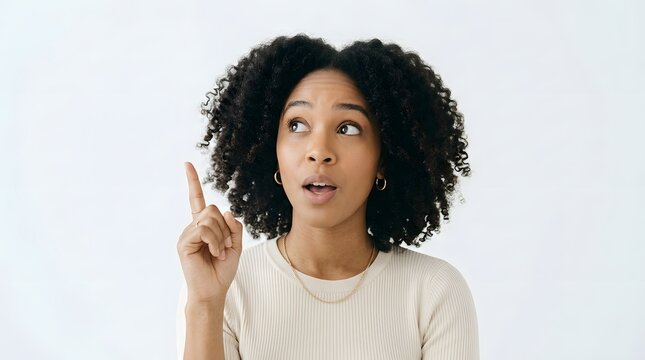 A young african american woman with beautiful curly hair suddenly has a bright idea and points upwards looking surprised and thoughtful