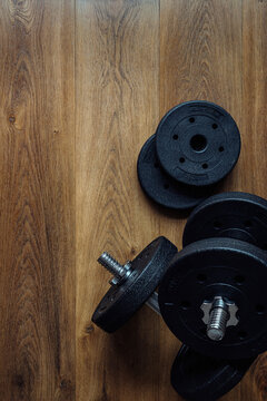 Black adjustable dumbbells and weight plates on a wooden floor background with copy space for fitness training design. Vertical format.