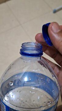 Close up of a person opening blue cap of plastic mineral water bottle during daily hydration routine indoors