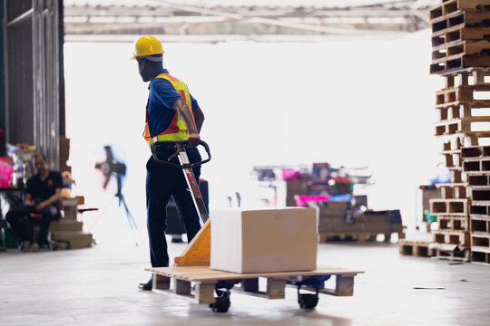 Warehouse worker in a blue polo and safety vest tows a pallet with one box across a distribution centre floor during a routine stock check in a distribution centre