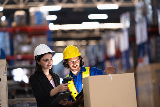 Bearded warehouse worker raises a hand in explanation while the manager scans a carton with a handheld reader while the supply chain team works a day shift in a warehouse