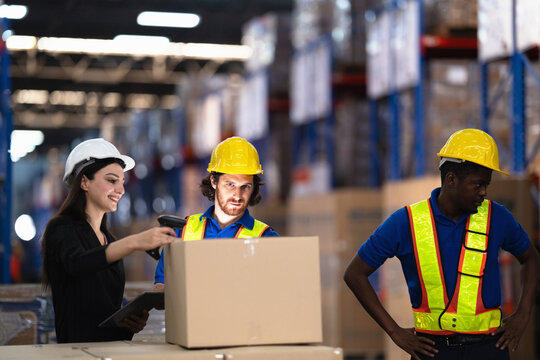 Warehouse manager points a handheld barcode reader at a carton as two workers watch the stock go in at a modern logistics warehouse handling storage shipping and delivery work